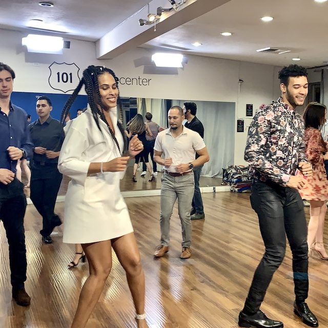A group salsa class dancing mid-lesson in a studio