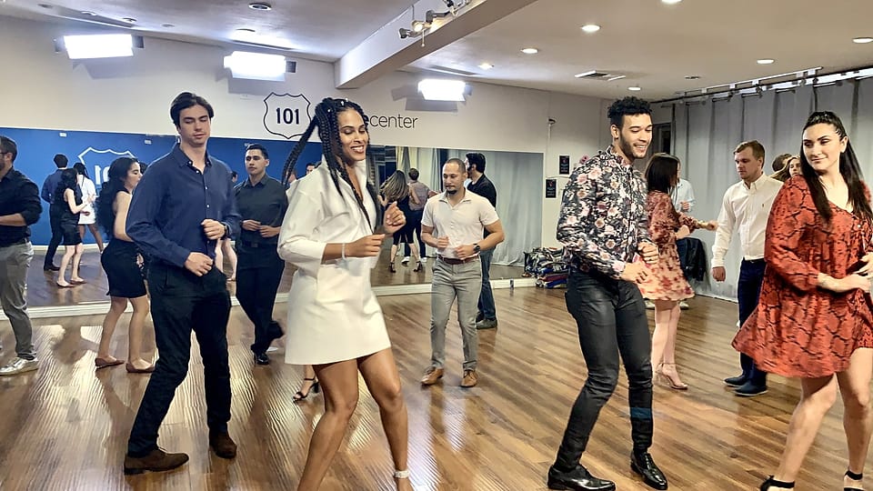 A beginner group learning salsa steps together in a studio